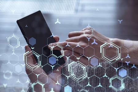 Programmer holding in the hands a smart phone and testing an innovative application to provide a completely new service. Close up shot. Hologram tech graphs. Concept of Dev team.の写真素材