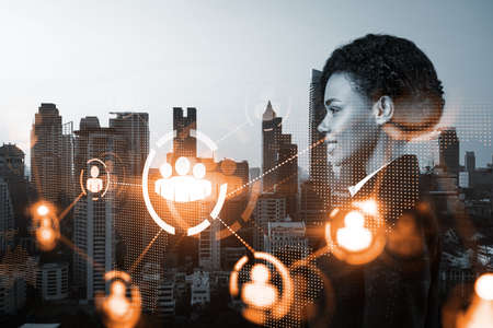 Attractive black HR director at international company is thinking about recruitment of highly qualified specialists. Women in business concept. Social media hologram icons over Bangkok.の写真素材