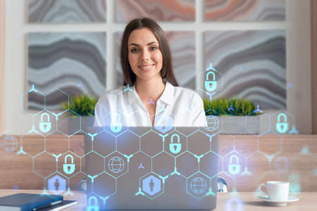 Attractive businesswoman in white shirt at workplace working with laptop to defend customer cyber security. Concept of clients information protection. Padlock hologram over office background.の写真素材