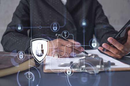 African American businesswoman in formal wear signing the contract to prevent probability of risks in cyber security. Checking the phone. Padlock Hologram icons over the working desk.の写真素材