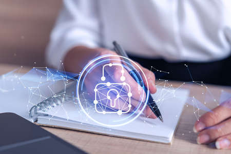 Businesswoman is taking notes of clients needs to protect cyber security from hacker attacks and save clients confidential data. Padlock Hologram icons over the typing hands. Formal wearの写真素材