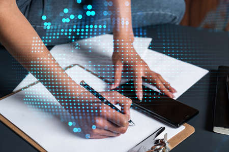 Businesswoman taking notes using smart-phone. World map hologram double exposure.の写真素材