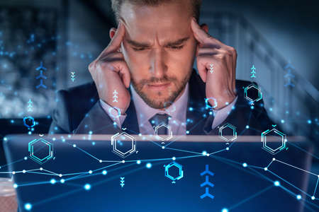 Handsome businessman in suit at workplace working with laptop to optimize development by implying new technologies in business process. Hi tech hologram over office backgroundの写真素材