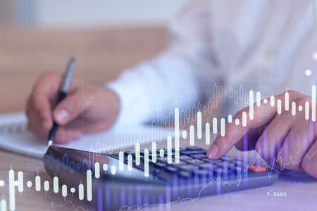 A trader computing historic data to predict stock market behavior. Internet trading concept. Forex and financial hologram chart over the desk and calculator.の写真素材
