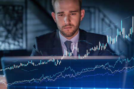 Handsome businessman in suit at workplace working with laptop to optimize trading strategy at...