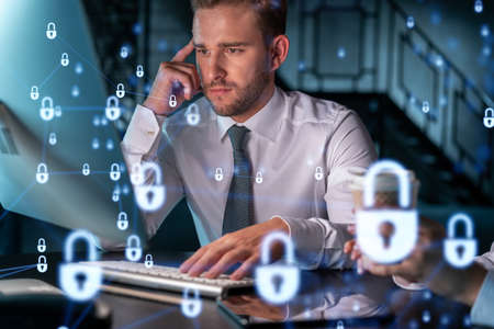 Two colleagues working together to protect clients confidential information and cyber security. IT hologram padlock icons modern office background at night timeの写真素材
