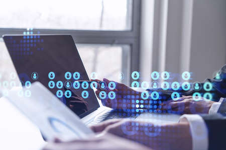Two HR specialists analyzing the recruitment market using laptop to boost the intern program at international consulting company. Social networking hologram icons.の写真素材