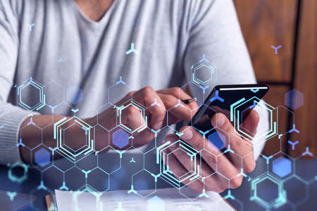 Programmer holding in the hands a smart phone and testing an innovative application to provide a completely new service. Close up shot. Hologram tech graphs. Concept of Dev team.の写真素材