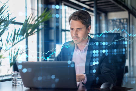 Handsome businessman in suit at workplace working with laptop to optimize trading strategy at...