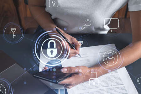 A businesswoman in casual wear signing the contract to prevent probability of risks in cyber security. Checking the phone. Padlock Hologram icons over the working desk. Women in business concept.の写真素材