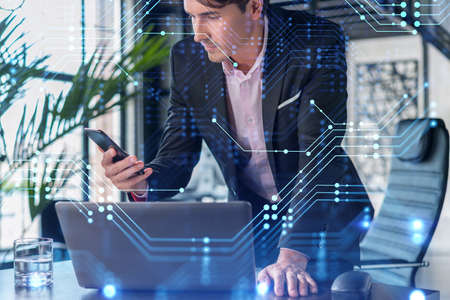 Businessman in suit using smart phone to optimize development by implying new technologies in business process. Interconnections and hi tech hologram over modern panoramic office background.の写真素材