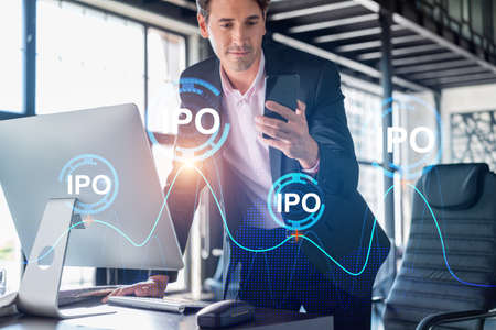 Businessman in suit using smart phone to optimize IPO strategy at corporate finance. Chart hologram over modern panoramic office backgroundの写真素材