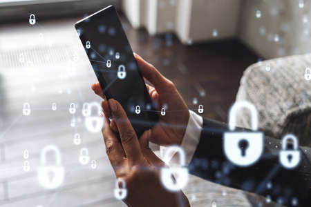 A woman programmer is browsing the Internet in smart phone to protect a cyber security from hacker attacks and save clients confidential data. Padlock Hologram icons over the typing hands. Formal wearの写真素材