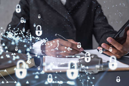 African American businesswoman in formal wear signing the contract to prevent probability of risks in cyber security. Checking the phone. Padlock Hologram icons over the working desk.の写真素材