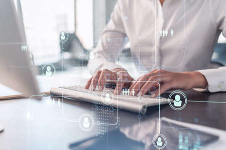 HR woman specialist is typing the keyboard in the internet to find the best candidates to create international network in recruitment process. Formal wear. Social media hologram icons.の写真素材