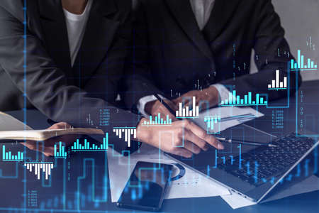 Two traders researching historic data to predict stock market behavior. Women in trading business concept. Forex and financial hologram chart over the table with the document.の写真素材