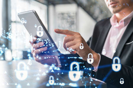Businessman in suit checking cyber security using tablet device to protect clients confidential information. IT hologram lock icons over modern panoramic office background.の写真素材