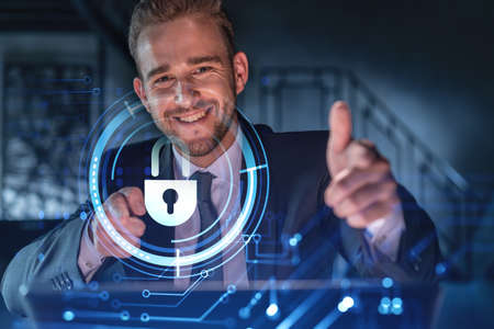 Portrait of handsome businessman thinking how to protect clients confidential information and cyber security. IT hologram padlock icons over office background.の写真素材