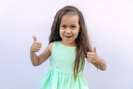 Little girl with brown long curly hair isolated on white background. Kid giving two thumbs upの写真素材