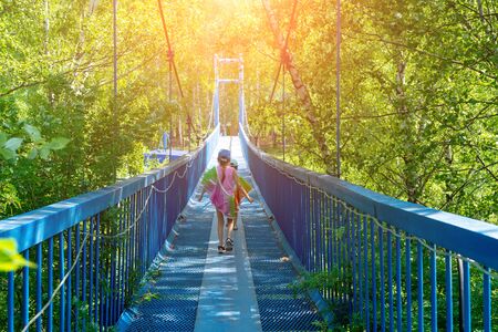 Two little happy girls walk along a hanging bridge on a sunny dayの写真素材