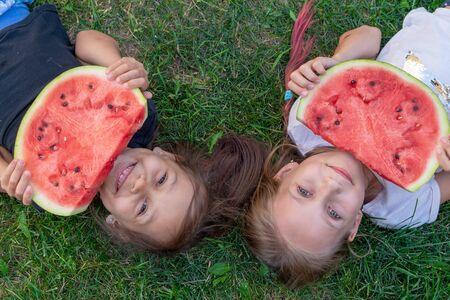 Two sisters summer portrait. smiling children outdoor. children with watermelon. Two happy smiling child eating watermelon in park. Concept of summerの写真素材