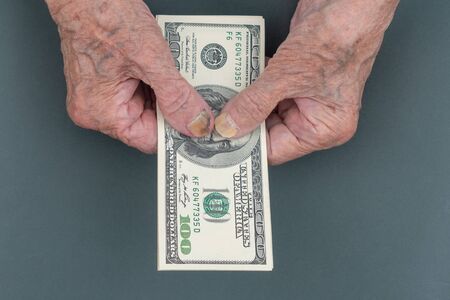 Poor elderly woman is counting some American Dollars in her hand. wrinkled Hands of an old woman. Counting money, economy concept, money sharing. Thrift. Financial supportの写真素材