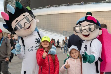 Russia, Kazan - August 27, 2019: Portrait of a smiling fans: Two adorable Russian white kid girls with animators with the logo of the Championship in the fan zone during the WorldSkills Kazan 2019 China Russia - Image. thumbs upのeditorial素材