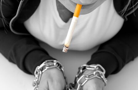 Womans hands tied by chain with cigarette on a white background. Stop smoking concept, cigarettes, A woman with red hair smokes a cigarette, hands tied with a chain. black and white.の写真素材