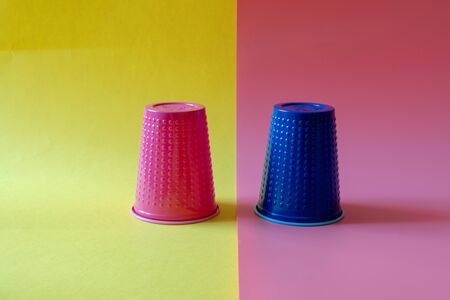 Multi-colored blue and pink plastic cups on a yellow and pink background. Plastic pollution concept