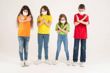 Group of schoolchildren children in colorful T-shirts and medical masks showing crossed hands gesture while looking at the camera over white background. Isolated. Stay at home. Say No to the coronavirusの写真素材