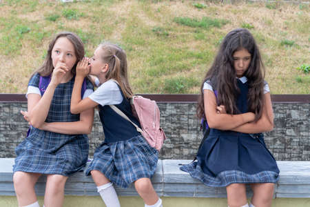 Three schoolgirls are sitting in the schoolyard. One child is offended. The problem of adaptation and communication at schoolの写真素材