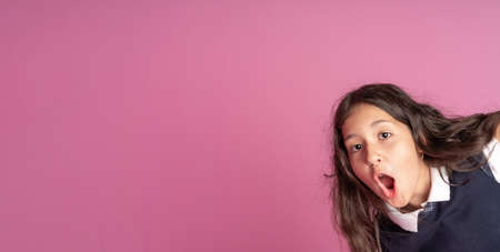 A charming girl with long curly dark hair in a school uniform with her mouth open with delight. Emotion of delight and surprise on your face. Studio photo. Back to school.の写真素材