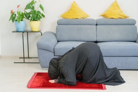caucasian Muslim Female Praying Sujud at home. A woman in a traditional black abaya and hijab prays...