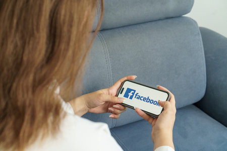 teenage girl with phone in her hands are sitting at home on bed. Social Media Facebook is loaded on screen. Turkey, Istanbul, September 17, 2024.のeditorial素材