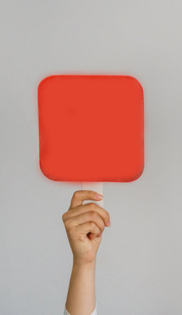 Female hand holding blank mock up banner sign as copy space for quotation text or graphic design. Sign red square in female hand on gray background.の写真素材