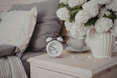 A serene morning scene featuring a white alarm clock, a cup of coffee, and a vase of white flowers...