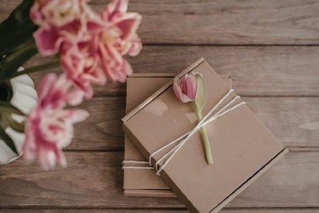 Two brown packages wrapped with twine and a pink flower on top, placed on a wooden table with pink...