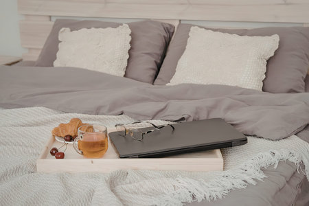 A breakfast tray with a laptop on a bed with grey and white bedding