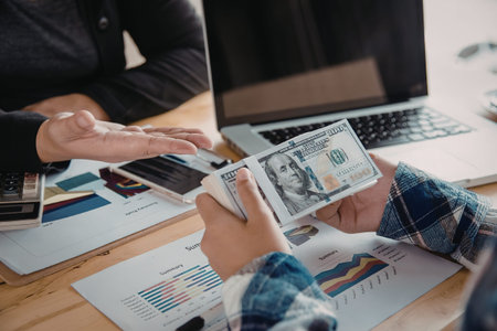 Two individuals sitting at a desk, examining financial documents and moneyの写真素材