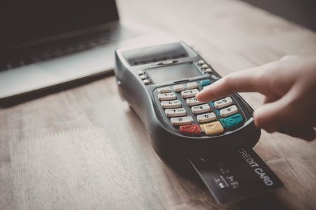 A person's hand is shown pressing a button on a payment terminal, with a credit card inserted and a...
