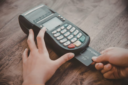 A person is shown making a payment using a credit card and a payment terminal on a wooden table.