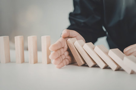 A person in a black shirt is stopping falling wooden dominoes with their hand on a white surface.