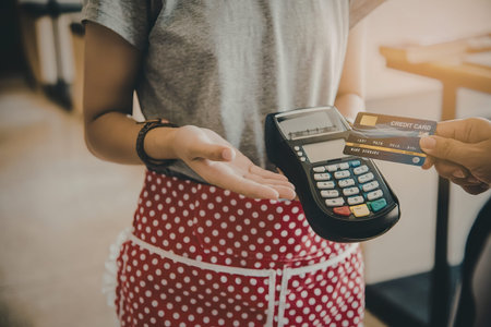 A woman wearing a red apron with white polka dots is making a payment using a credit card through a...