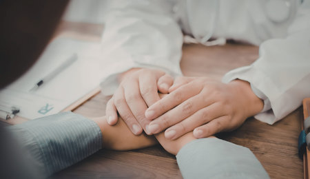 A doctor in a white coat places a comforting hand on the wrist of a patient, conveying empathy and...