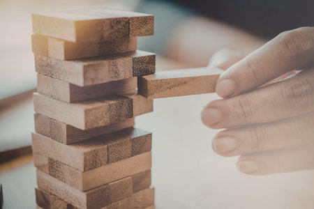 A person's hand pulling out a wooden block from a tower game, with the tower standing on a table and...