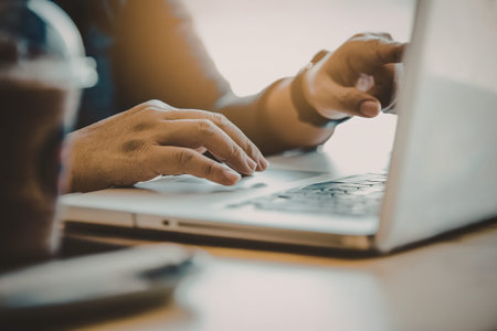 A person typing on a laptop with a cup of coffee nearby