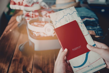 A person's hands holding a red passport and a map, with a blurred background of a table with items.
