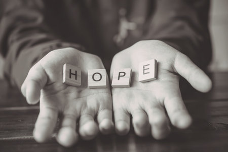 A pair of hands holding the word 'HOPE' made of letter tiles