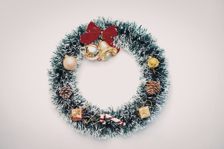 A Christmas wreath made of green tinsel with various ornaments, including gold balls, pinecones, and candy canes, topped with a red bow.の写真素材