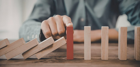 A person stopping a domino effect with a red block, symbolizing crisis management or prevention.